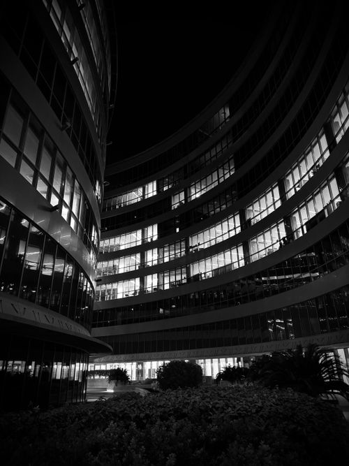 Free Black and white photo of a curved modern building at night. Illuminated windows add depth. Stock Photo
