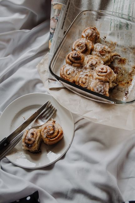 A 9x13 baking dish of golden overnight Rhodes cinnamon rolls drizzled with white vanilla glaze, one roll pulled apart to show the soft interior.