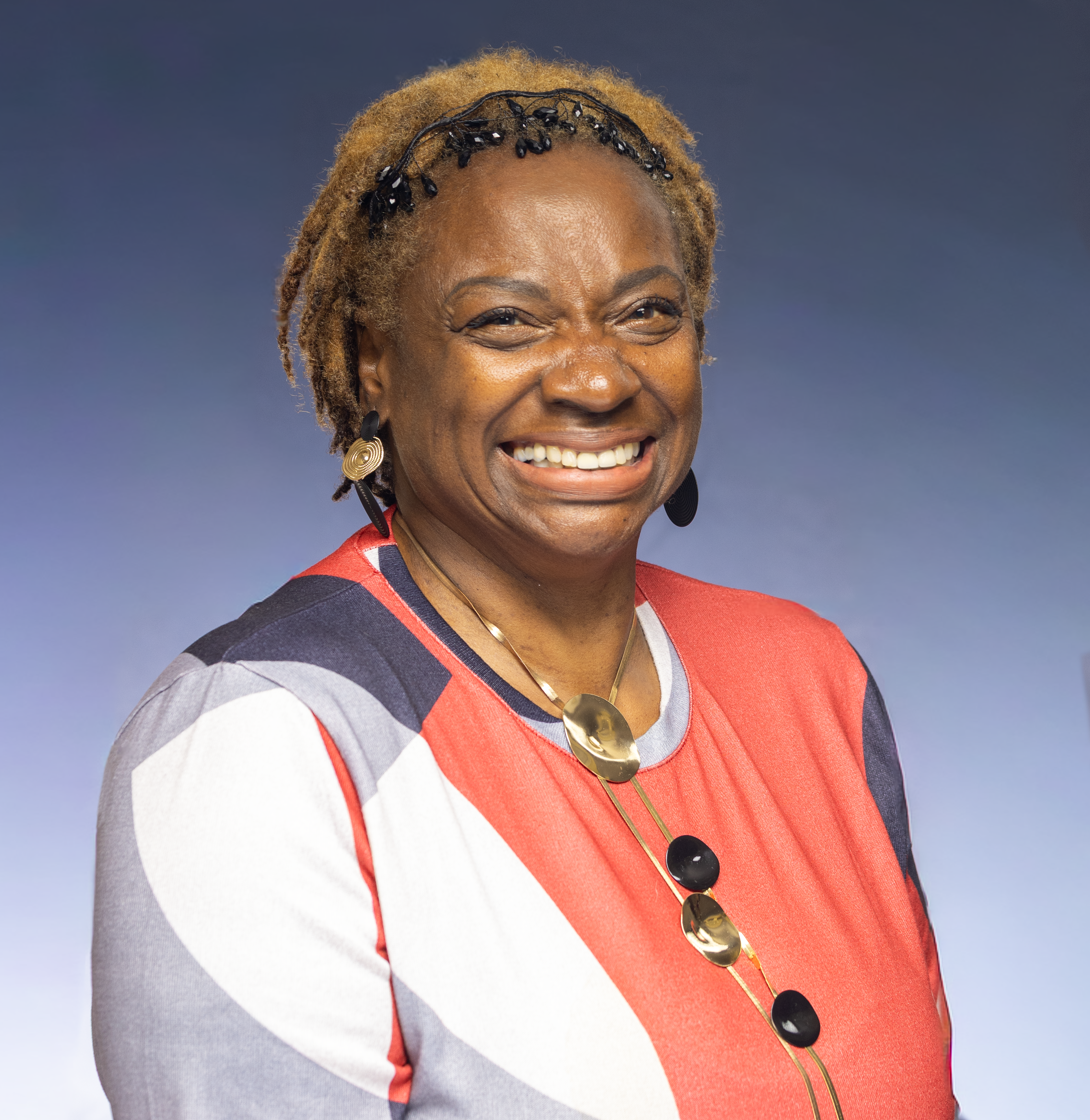 Smiling woman wearing a colorful geometric dress and unique jewelry, exuding joy.