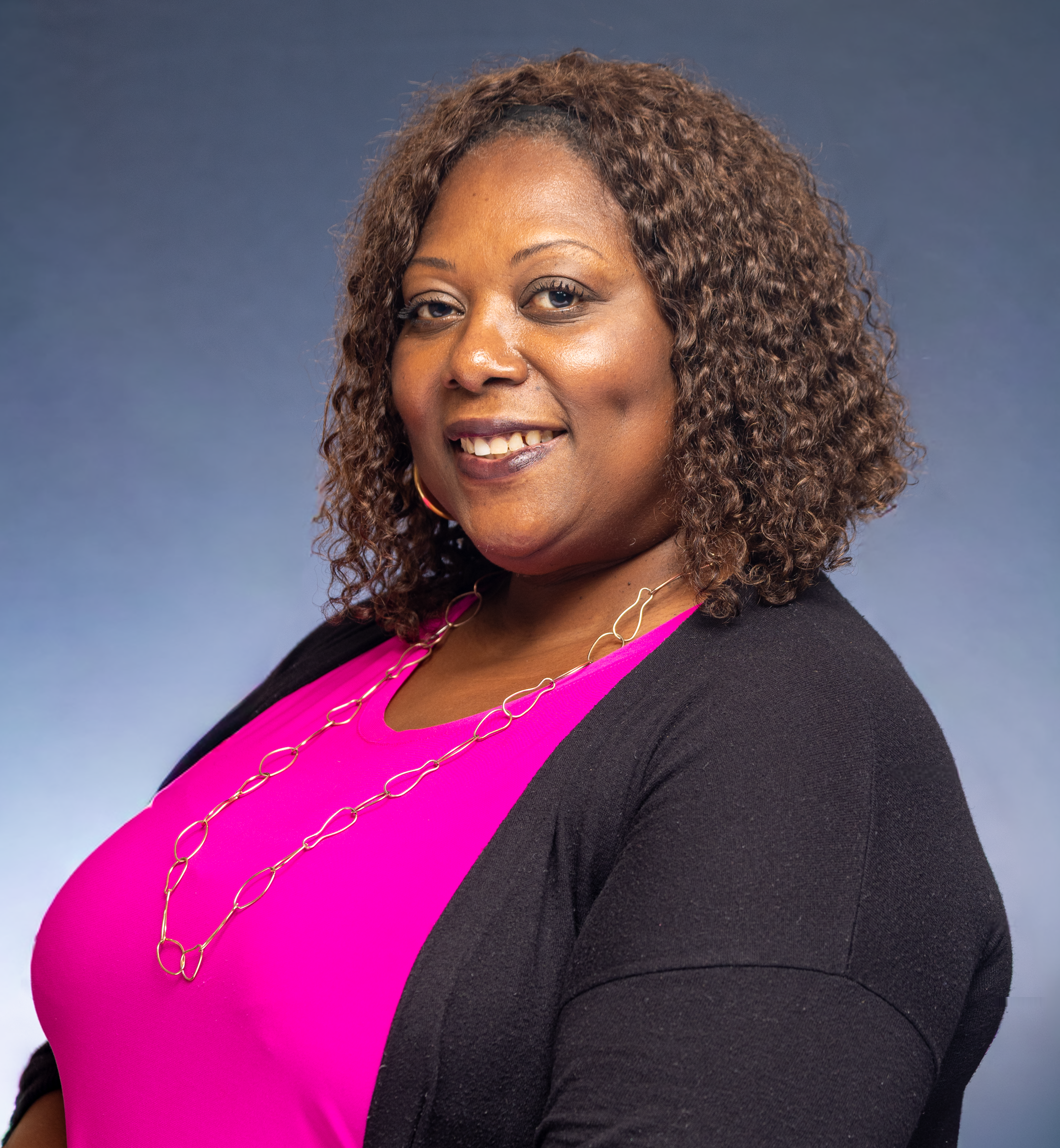 Portrait of a smiling woman in a pink top with curly hair against a neutral background.