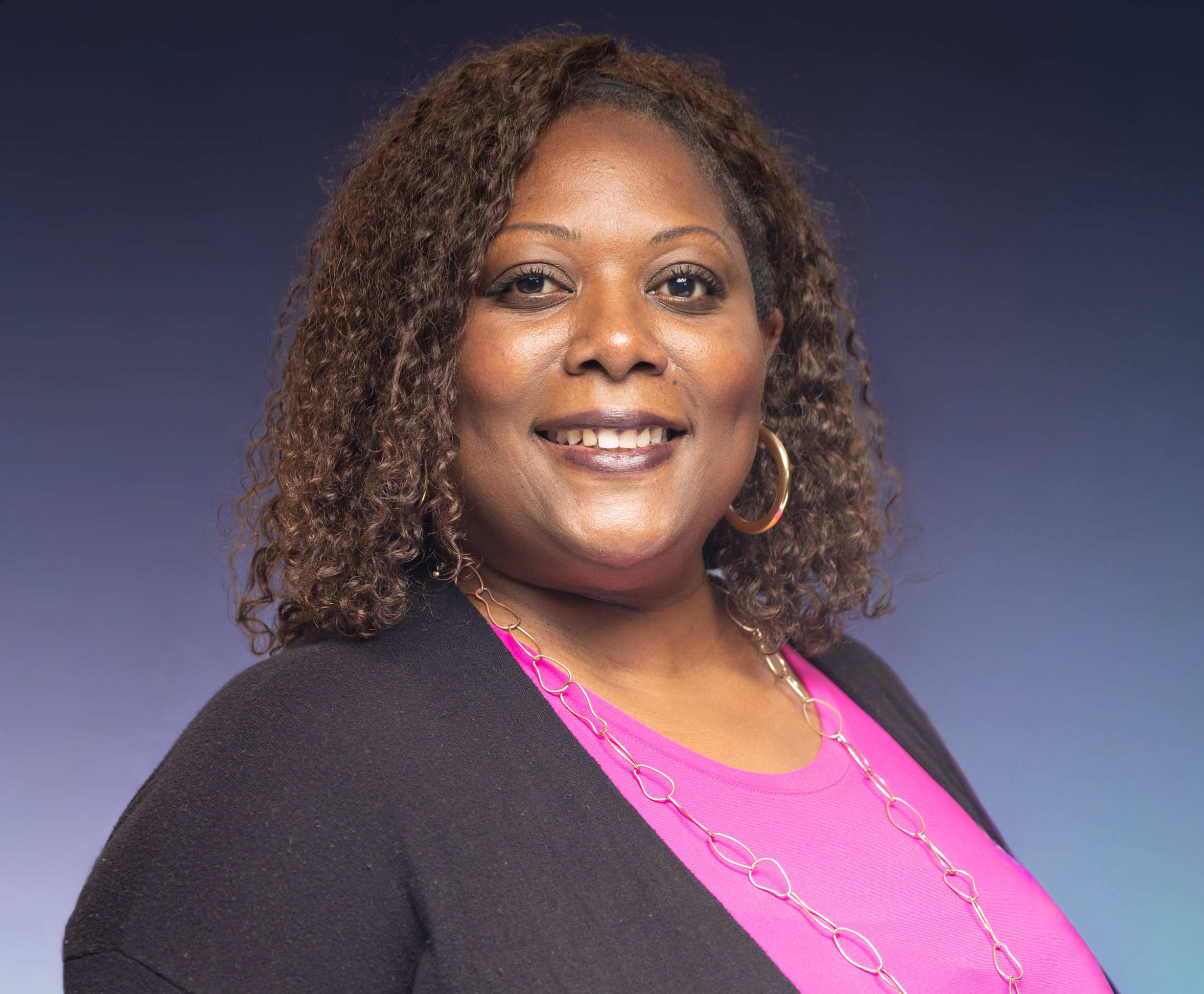 Confident woman smiling in stylish pink top and black cardigan against blue background.