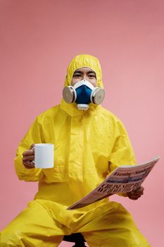 一个穿着安全服、戴着口罩的人拿着杯子在读报纸