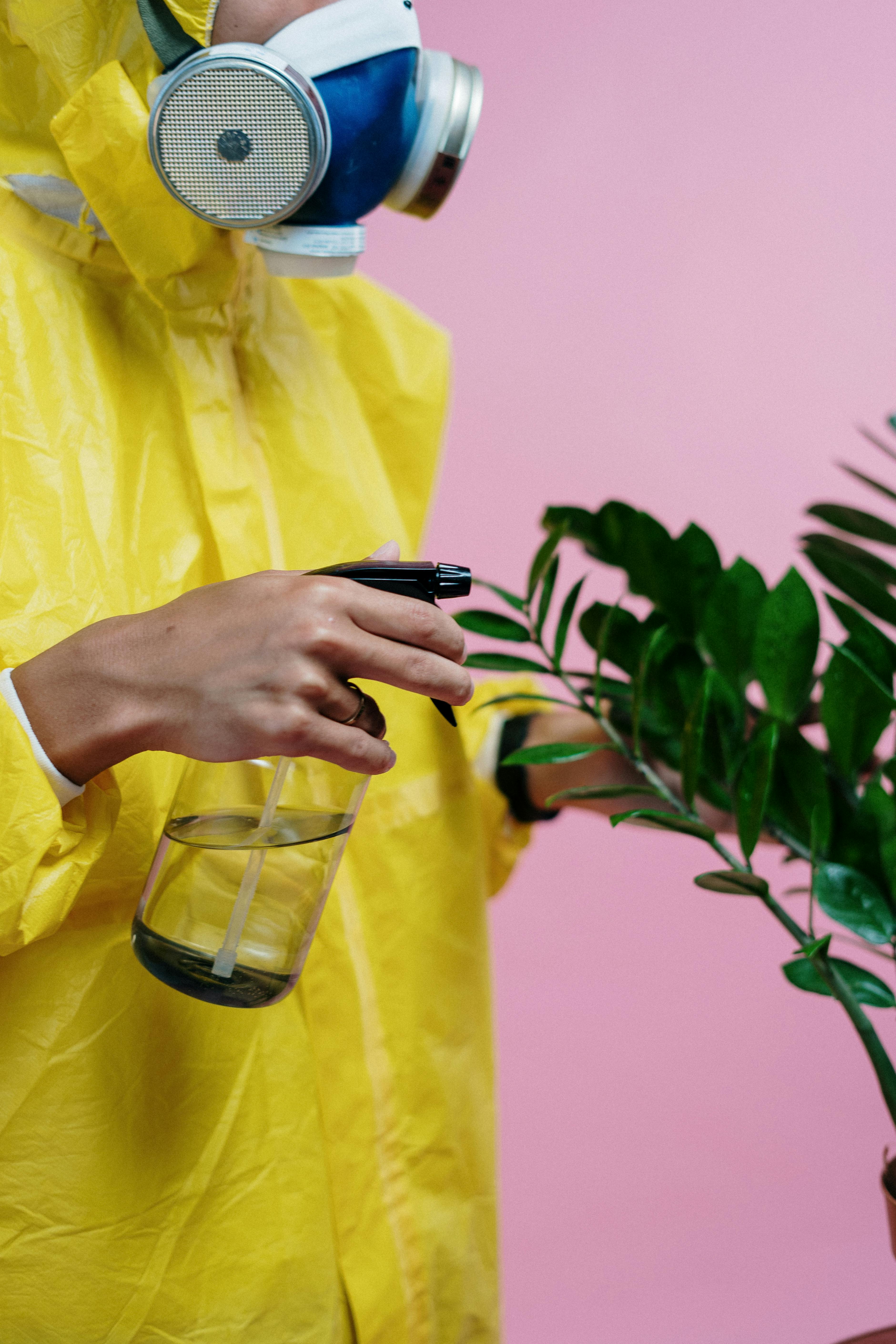 person in yellow protective suit watering a plant