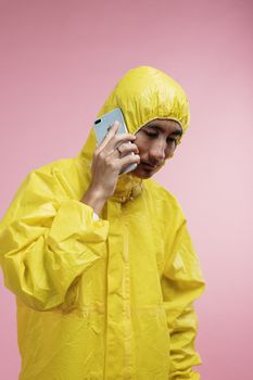 一名身穿黄色防护服的亚洲男子正用智能手机通话，背景是粉色