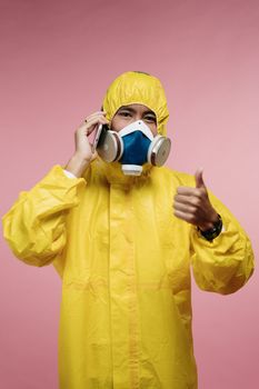 穿着黄色防护服、戴着呼吸器的成年人竖起大拇指打电话