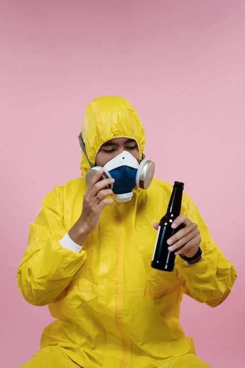 Free A man in a yellow hazmat suit humorously drinks beer against a pink background. Stock Photo