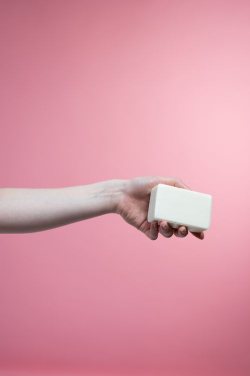 Free A hand holding a bar of soap with a pink background, symbolizing hygiene and cleanliness. Stock Photo