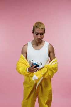 一名成年男性身穿黄色防护服，在粉色背景下手持呼吸器