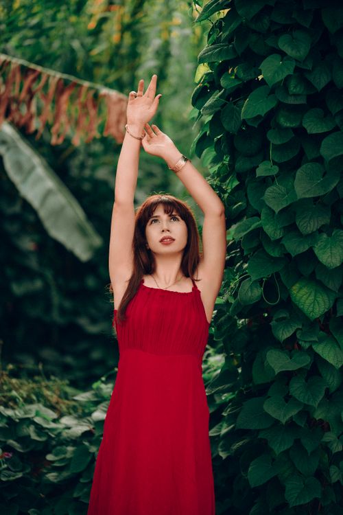 Free Young woman in red dress posing in a vibrant garden setting. Stock Photo