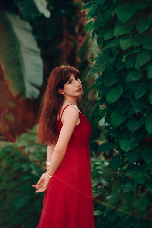 Free Elegant woman in a red dress poses amid tropical greenery, creating a striking contrast. Stock Photo