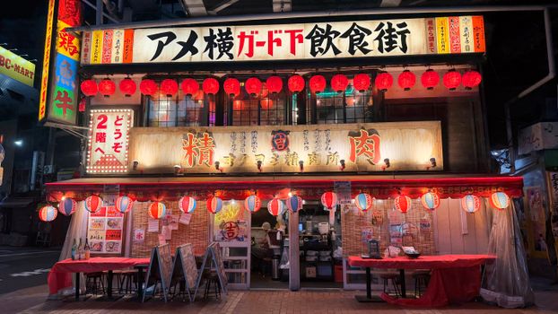 Traditional Japanese izakaya with red lanterns in a lively night setting.