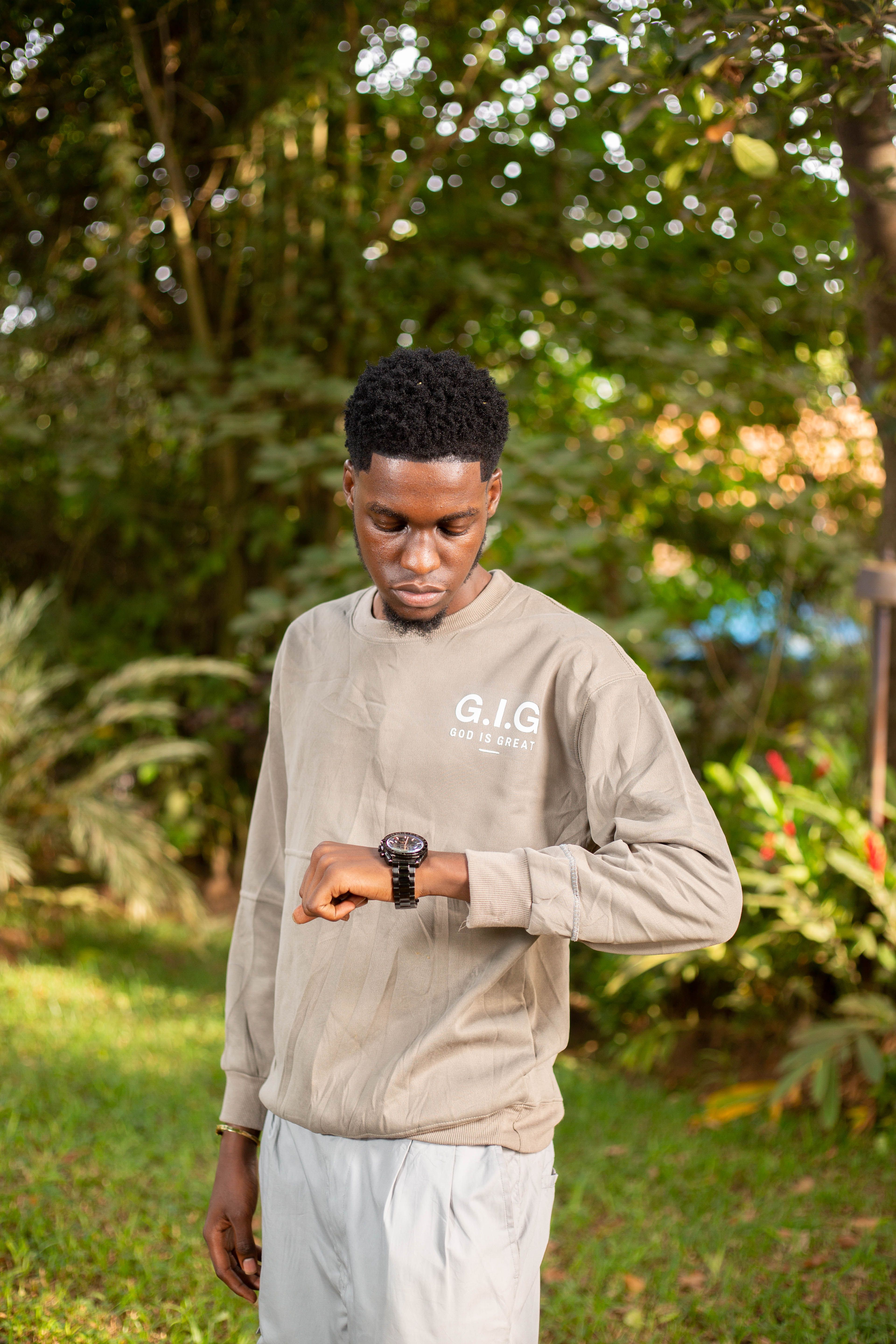 A young man in casual wear checks the time on his wristwatch in a vibrant garden setting.