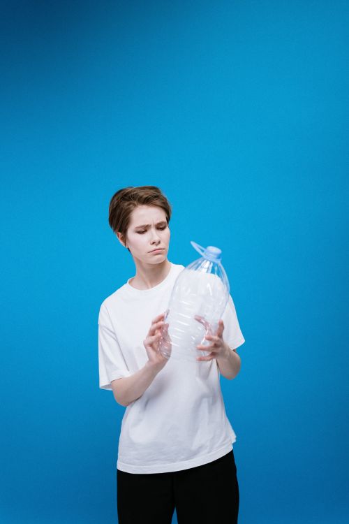 Free A young woman holding and examining a plastic bottle against a vibrant blue background, highlighting themes of recycling and pollution. Stock Photo