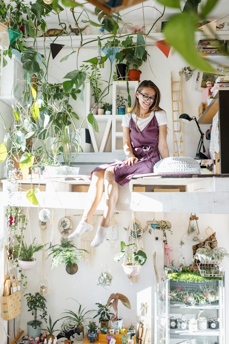 Young Woman Sitting In Apartment On Second Level With Plants