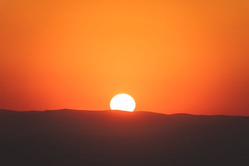 Free A tranquil sunset over desert dunes with vibrant orange and red hues illuminating the sky. Stock Photo