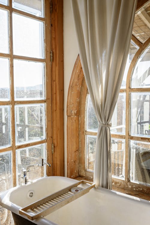 From above of bathtub in light bathroom with big shabby windows in vintage interior