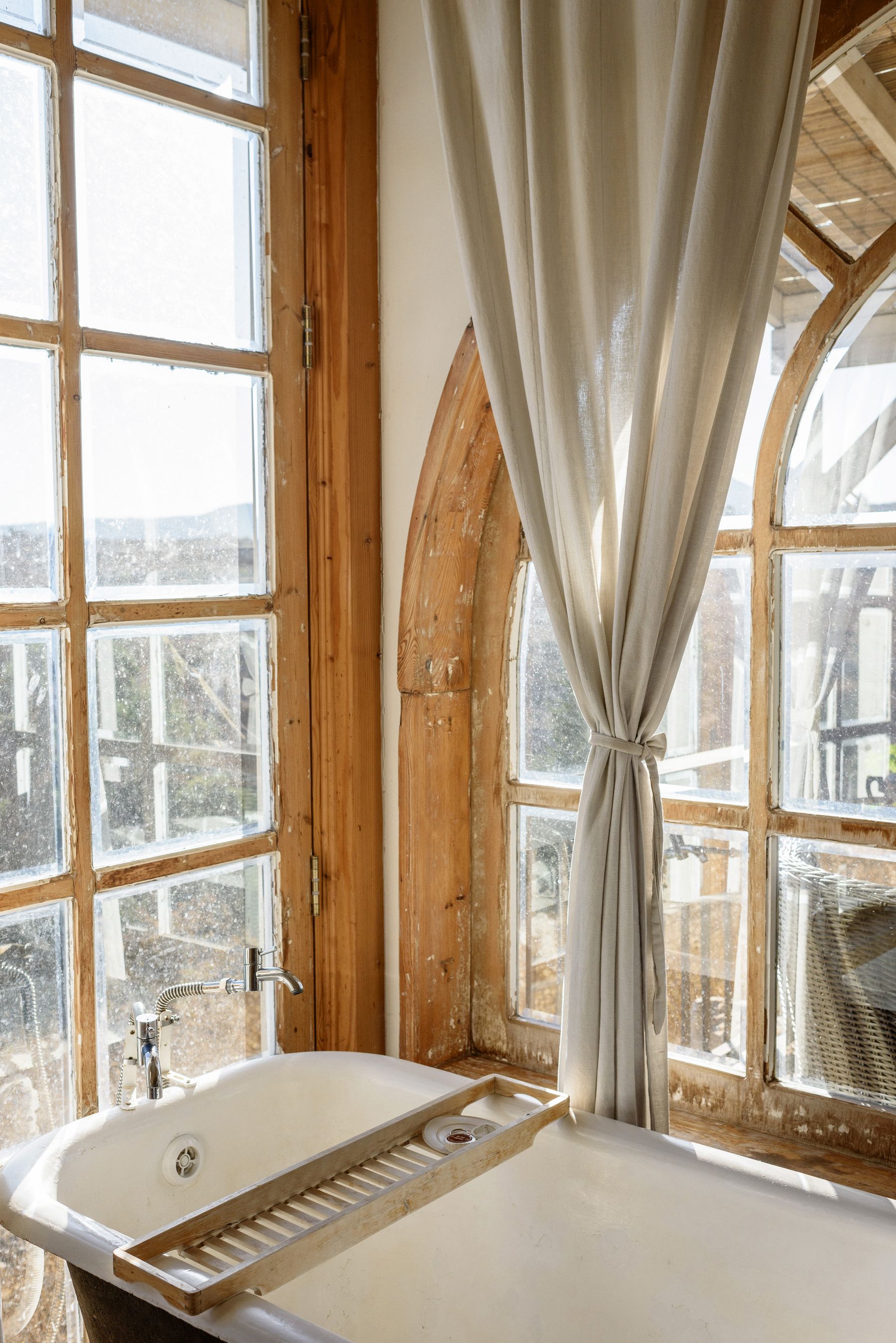 Sunlit classic room with large wood windows, pale surfaces and freestanding bath