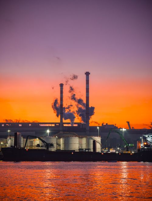 Free Silhouette of a harbor with ships and smokestacks against a vibrant sunset sky. Stock Photo