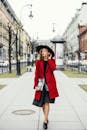穿着红色外套、戴着黑色帽子的时尚女子漫步在城市街道上