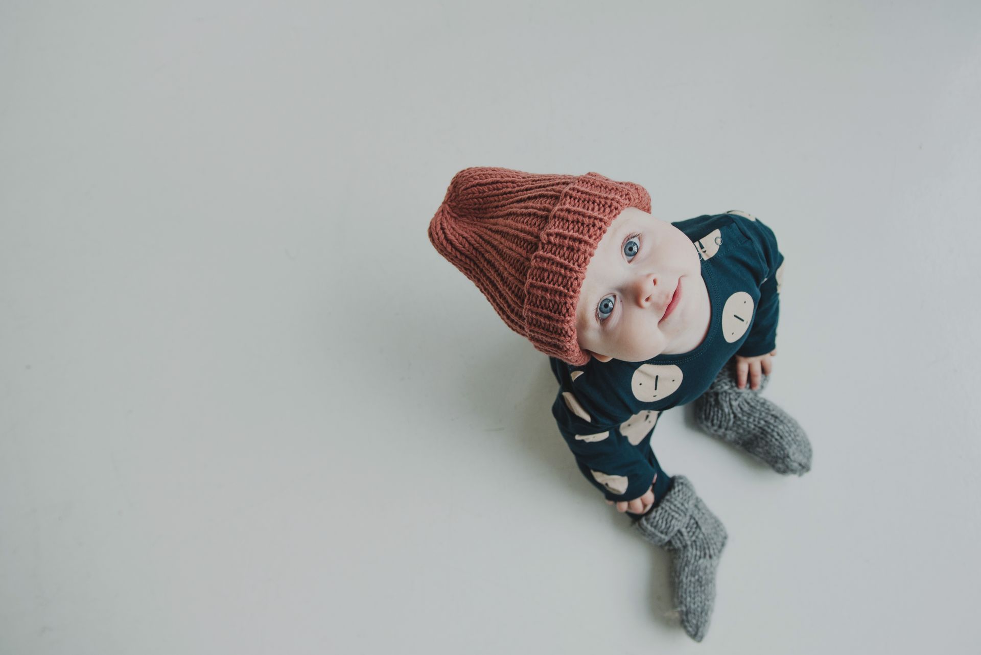 Cute baby wearing a knitted hat and socks, sitting on a light background.