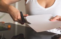 Close-up of a woman cutting white paper with scissors, highlighting precision and creativity in crafting.