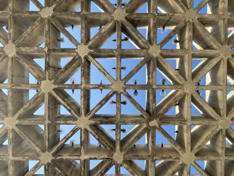 Perspective view of a geometric concrete ceiling with grid pattern against blue sky.