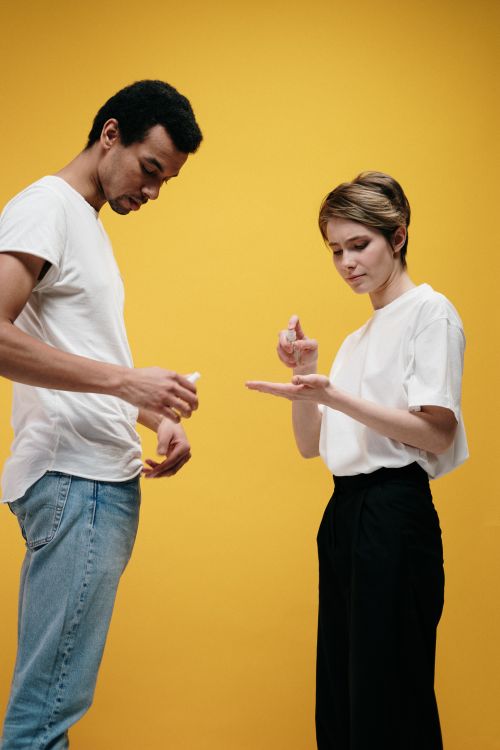 Free Young couple applying hand sanitizer on a vibrant yellow background for health and safety. Stock Photo