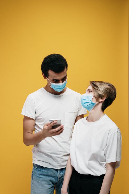 Free A couple with face masks using a smartphone against a yellow background, emphasizing technology and safety. Stock Photo