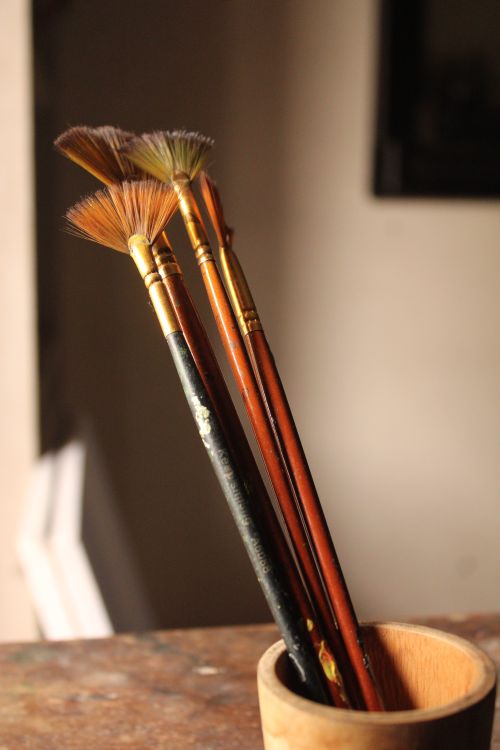 Free A set of fan paintbrushes in a wooden holder warmly lit by natural light. Stock Photo