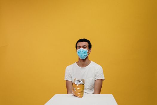 一名男子在隔离期间戴着口罩享用零食，展现了疫情下的生活方式