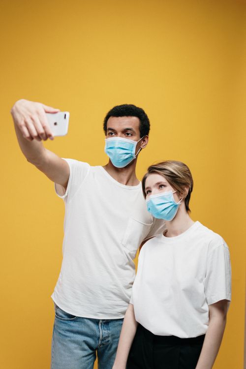 Free Couple wearing face masks takes selfie against yellow background during COVID-19 pandemic. Stock Photo