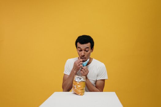 Man humorously eating chips while wearing a mask in a studio setting.