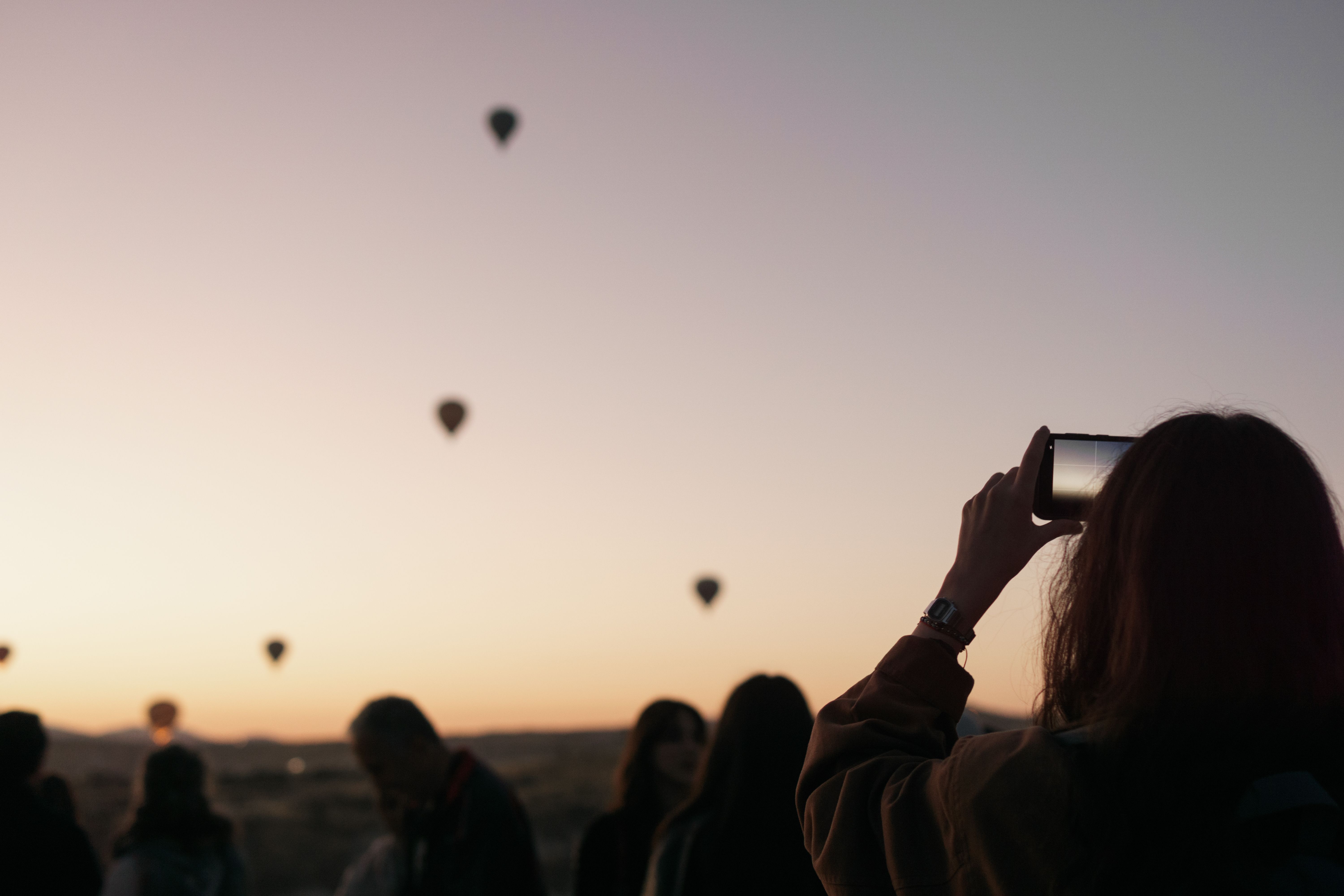 Silhouette of people capturing hot air balloons in Cappadocia at sunrise.