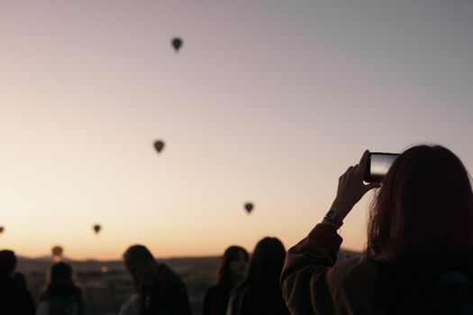 Silhouette of people capturing hot air balloons in Cappadocia at sunrise.
