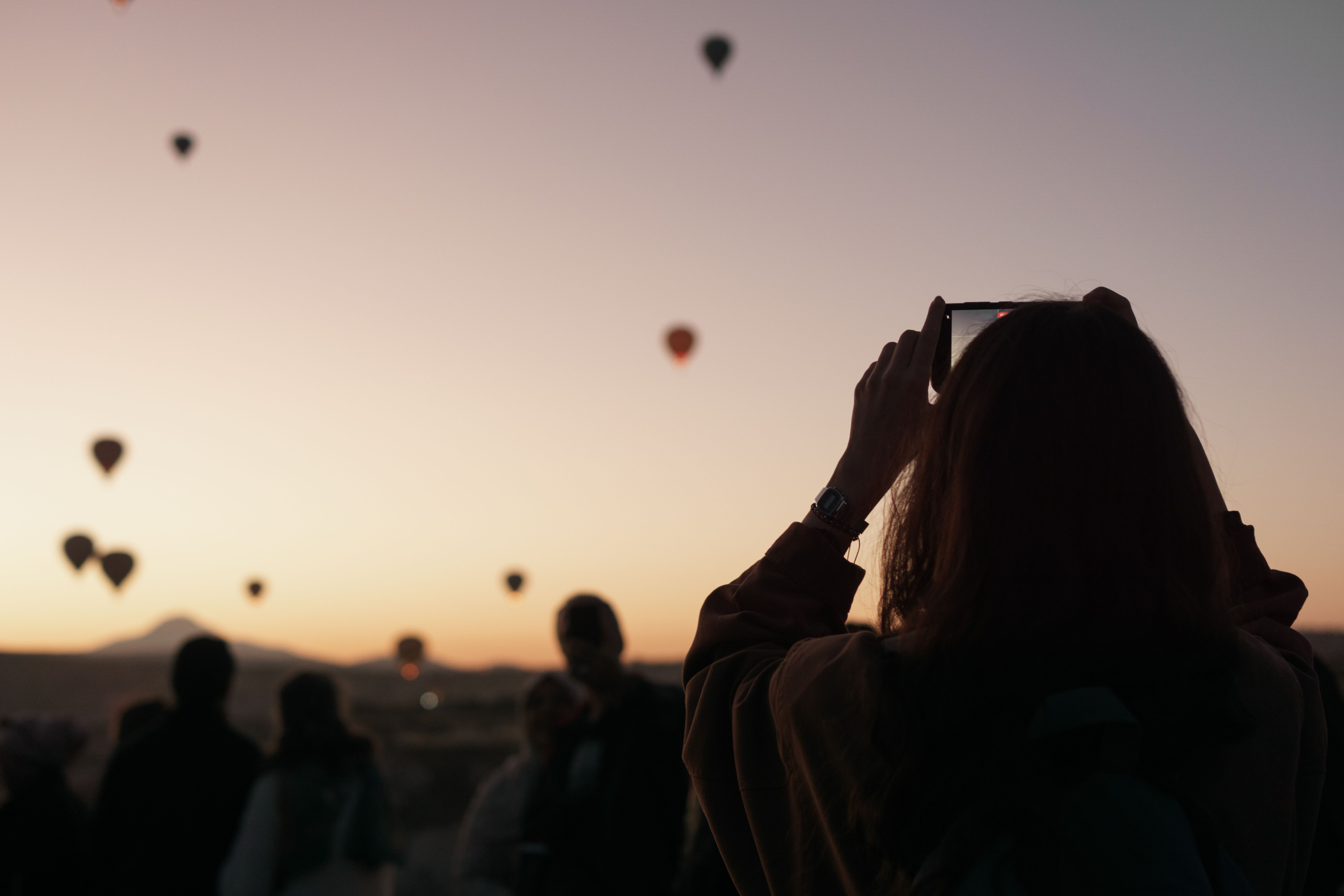 Woman takes a picture of hot air balloons at sunrise in Cappadocia, Türkiye.