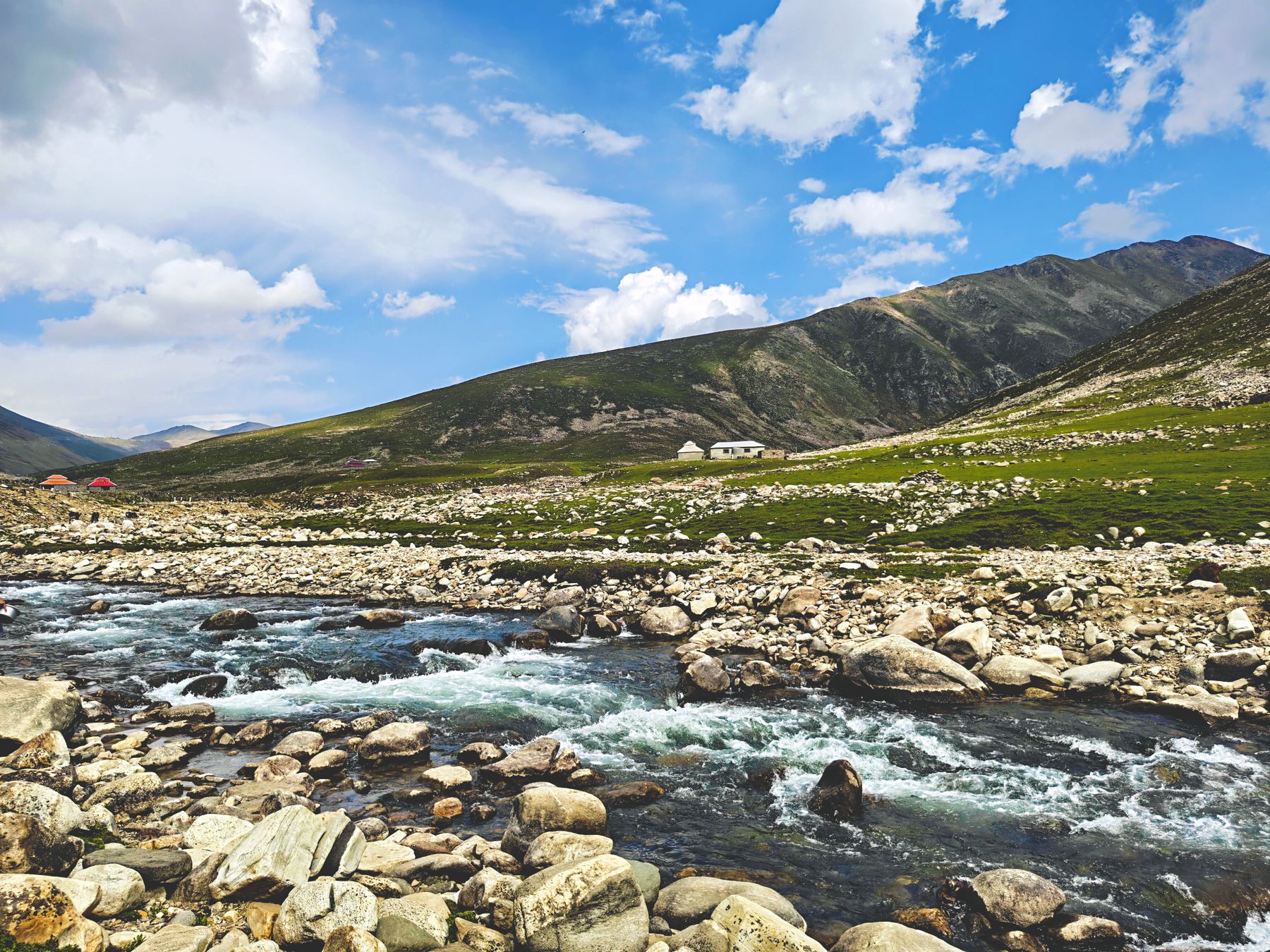 Crystal clear stream flowing through rocky landscape in Gittidas, Khyber Pakhtunkhwa, Pakistan, under a vibrant blue sky.