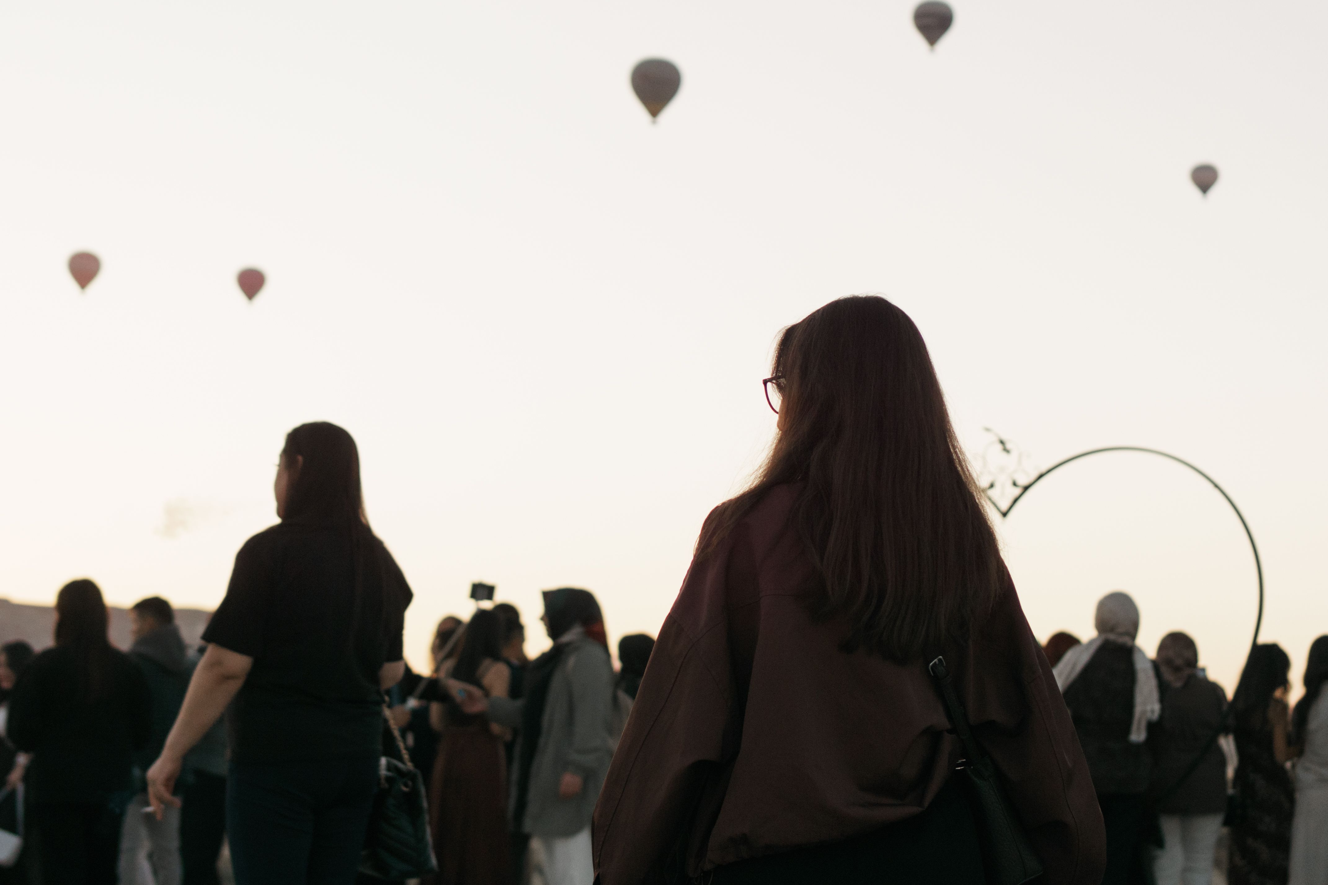Hot air balloons rise in Cappadocia at sunrise as a crowd gathers below, creating a picturesque scene in Türkiye.
