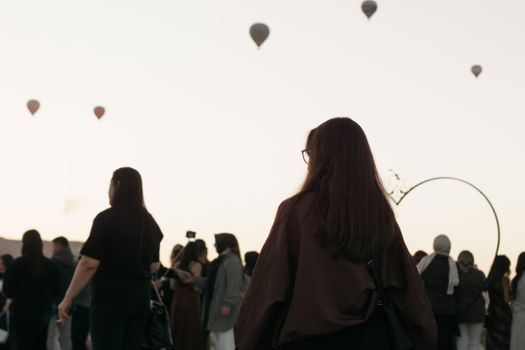 Hot air balloons rise in Cappadocia at sunrise as a crowd gathers below, creating a picturesque scene in Türkiye.