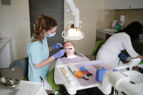 Woman In Blue Scrub Suit Checking A Patient's Teeth