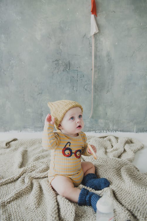 Free Baby in Yellow and Gray Stripe Onesie Sitting on Gray Knitted Textile Stock Photo