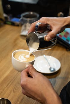 A barista expertly creates latte art in a fresh cup of coffee in a cozy cafe setting.