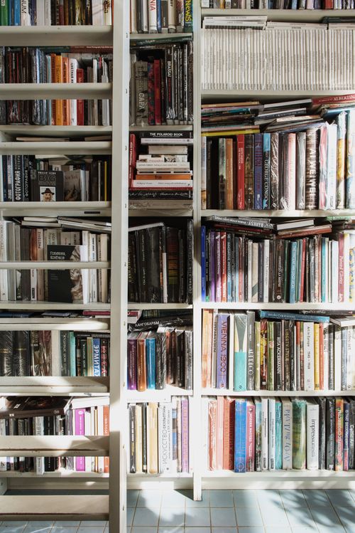Free A bookshelf packed with a variety of colorful books illuminated by sunlight, indoor library setting. Stock Photo