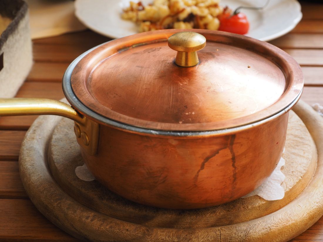 Copper saucepan with lid and brass handle on a round wooden trivet