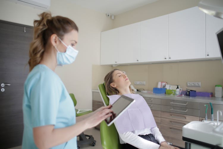 Female Orthodontist Using Tablet While Assisting Patient In Clinic