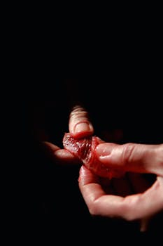 Detailed view of hands squeezing a juicy blood orange slice against a dark background.
