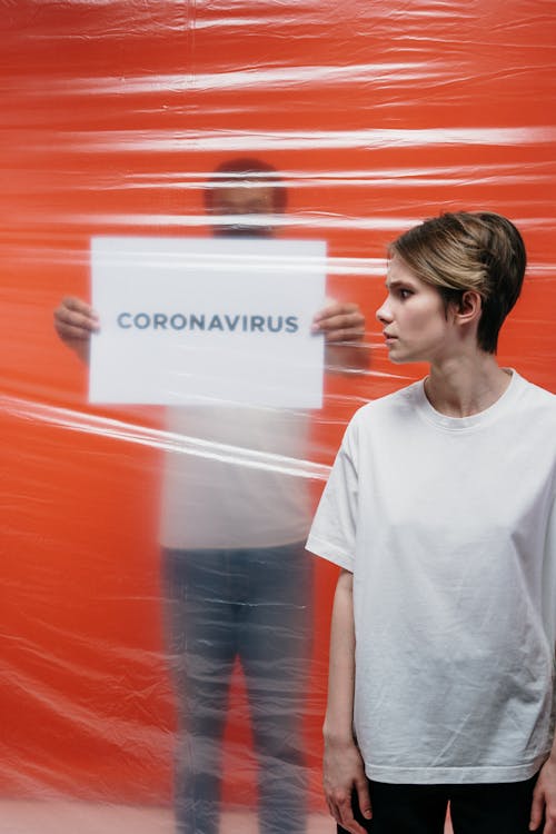 Free Woman With A Stressful Look At A Man Holding A Poster With Coronavirus Text Stock Photo