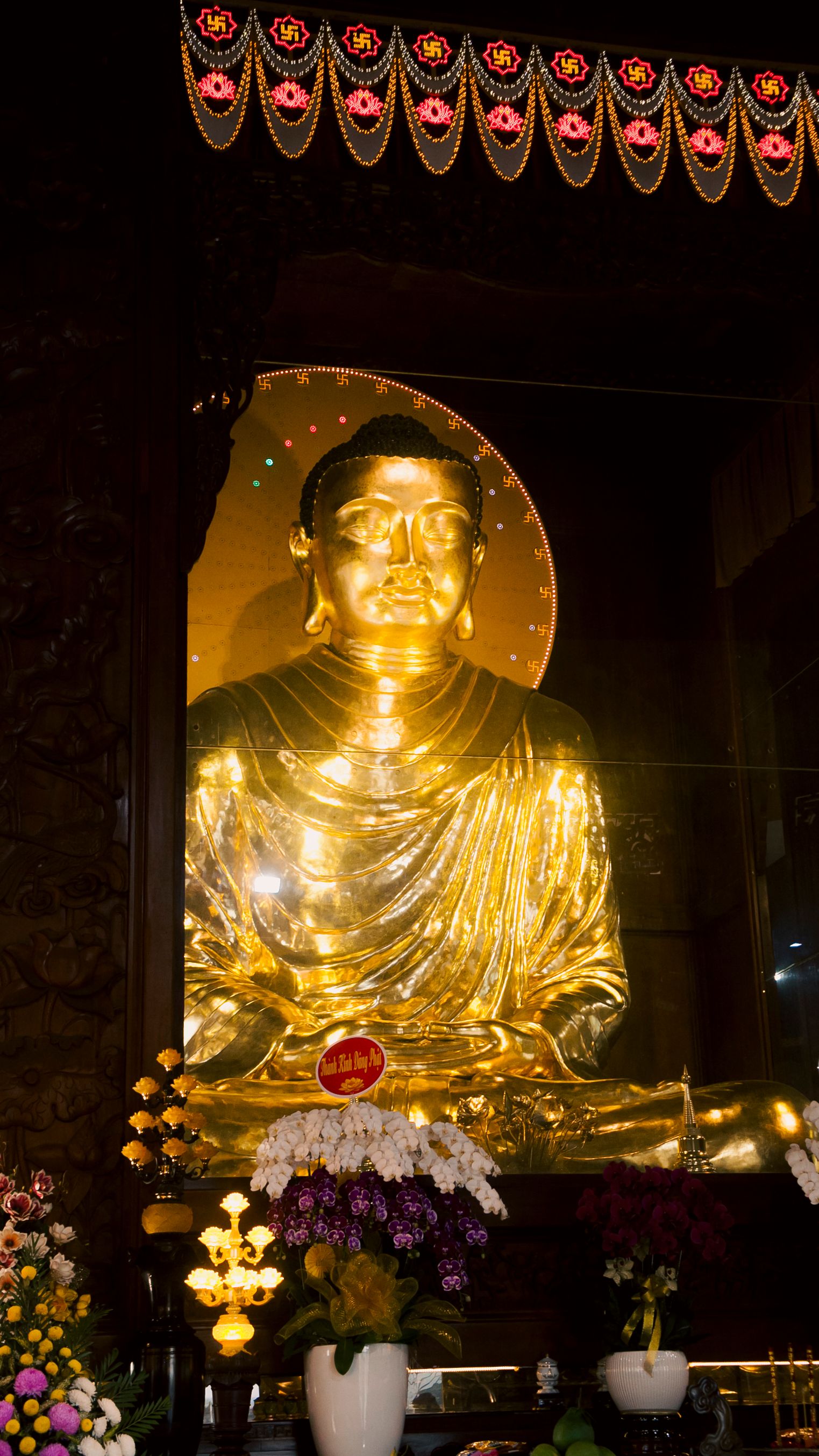 Majestic golden Buddha statue illuminated with flowers in Ho Chi Minh City temple.