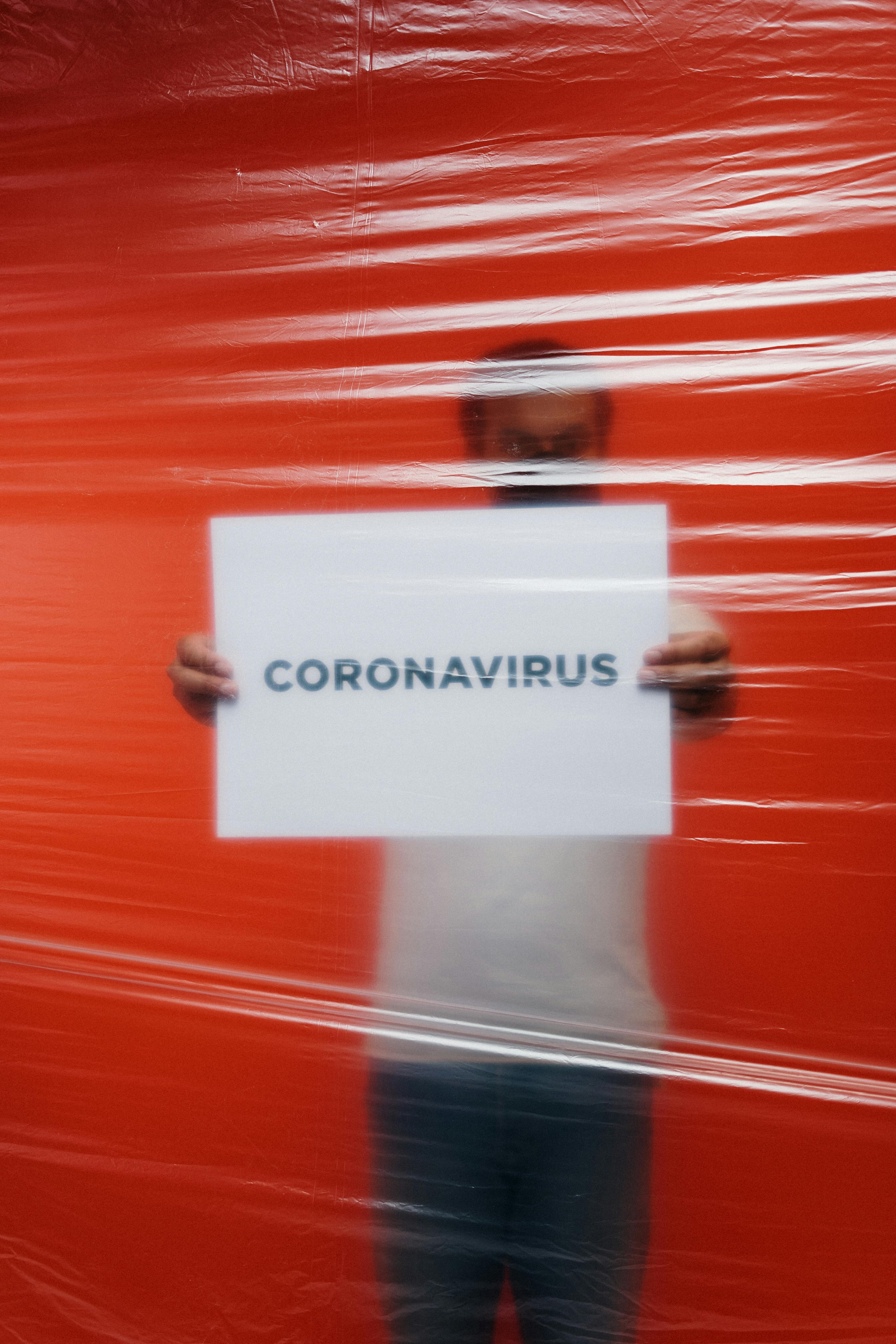 man holding a coronavirus sign behind a plastic