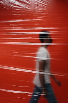 Silhouette of a man walking behind a translucent plastic sheet with an orange backdrop, creating a motion blur effect.