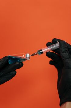 特写：一只戴着黑手套的手正从小瓶中吸取液体的注射器